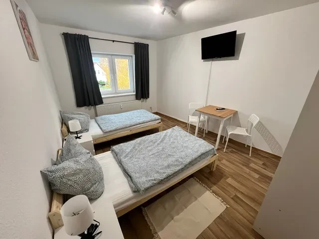 Großes Apartment mit zwei Einzelbetten, Tisch und Fernseher Modernes, großes Apartment mit zwei Einzelbetten, Holzfußboden, Tisch, Stühlen und Fernseher