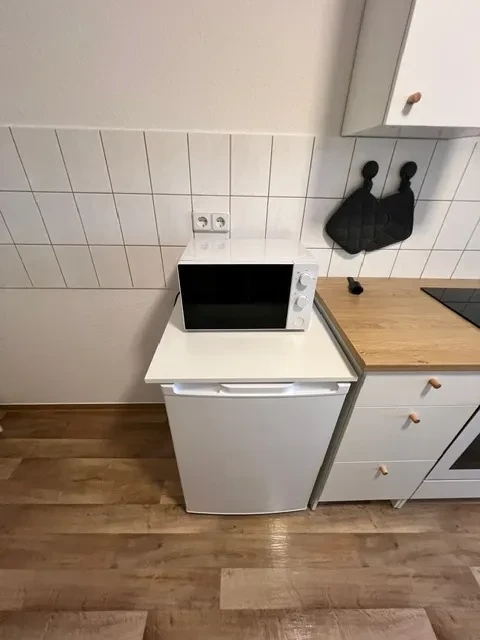 Küche im Apartment – Mikrowelle, Kühlschrank und moderne Ausstattung Küchenausstattung im Apartment mit Mikrowelle auf Kühlschrank und moderner Küchenzeile