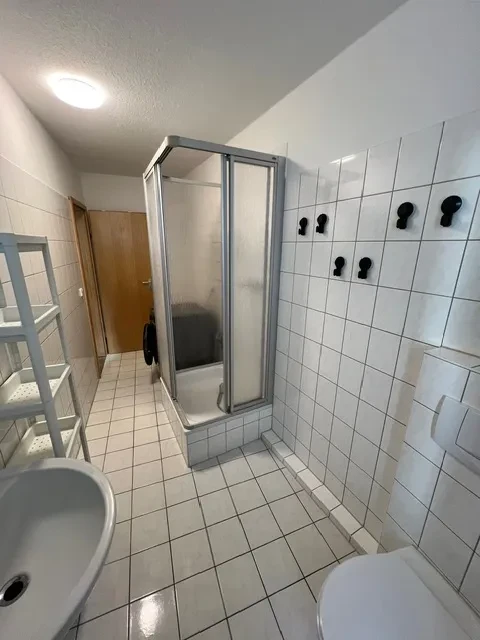 Badezimmer eines großen Apartments mit Dusche und weißen Fliesen Badezimmer in einem großen Apartment mit Dusche, weißen Fliesen und Ablagefächern