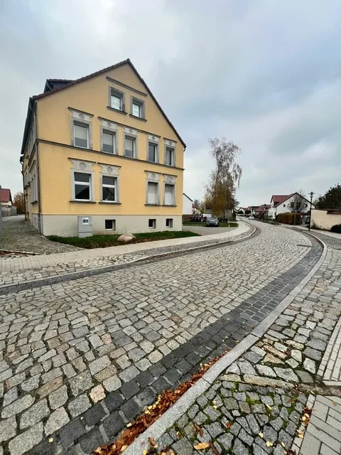 Mehrfamilienhaus in ruhiger Wohnlage mit gepflasterter Straße Gelbes Mehrfamilienhaus an einer gepflasterten Straße in ruhiger Wohngegend