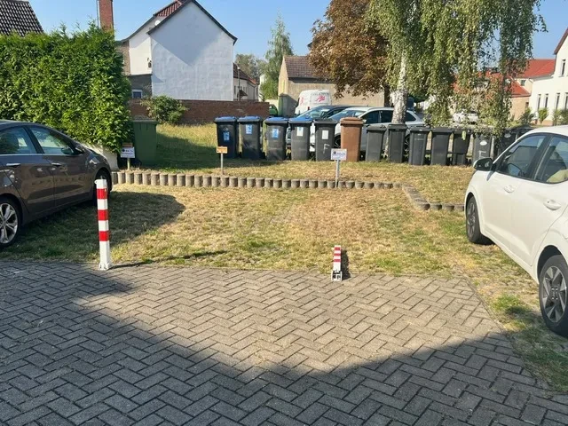 Parkplatz und Mülltonnen vor Apartment – apartment-gross-22.webp Parkplatz vor einem Apartmentgebäude mit Mülltonnen im Hintergrund, aufgenommen an einem sonnigen Tag