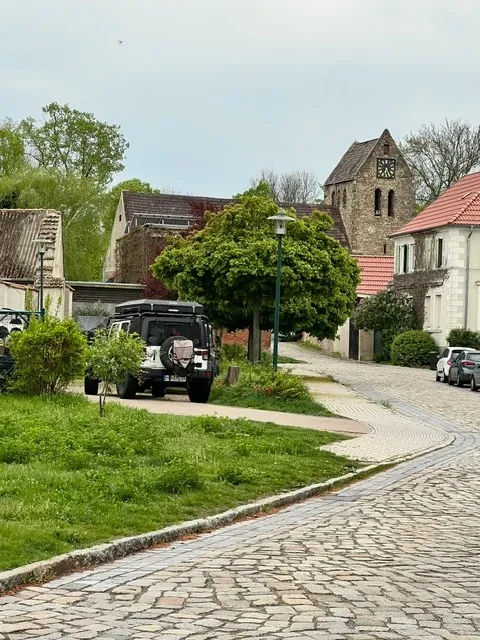 Idyllische Straße mit Kirche und Natur Ansicht einer ruhigen Kopfsteinpflasterstraße mit Kirche und geparkten Autos im Grünen