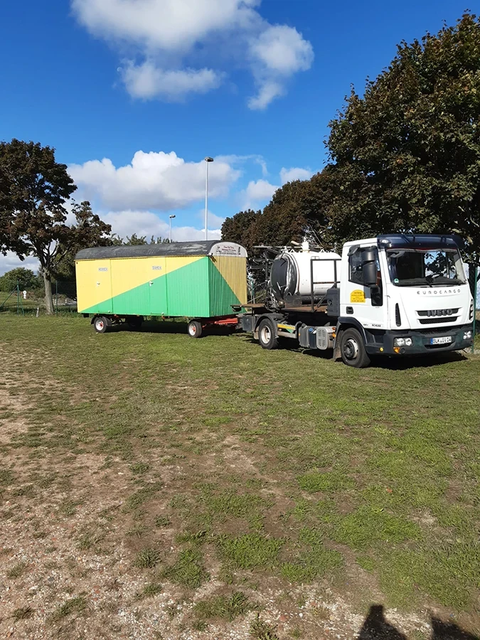 Döring Rohrreinigung und Abflussreinigung – Spezialfahrzeug auf Wiese vor grün-gelbem Container