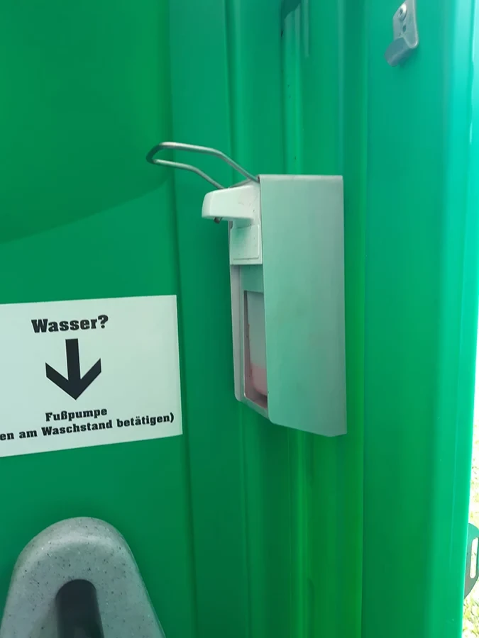 Doering Rohrreinigung Toilettenvermietung: Waschstand mit Seifenspender und Hinweis auf Fußpumpe in mobiler Toilette