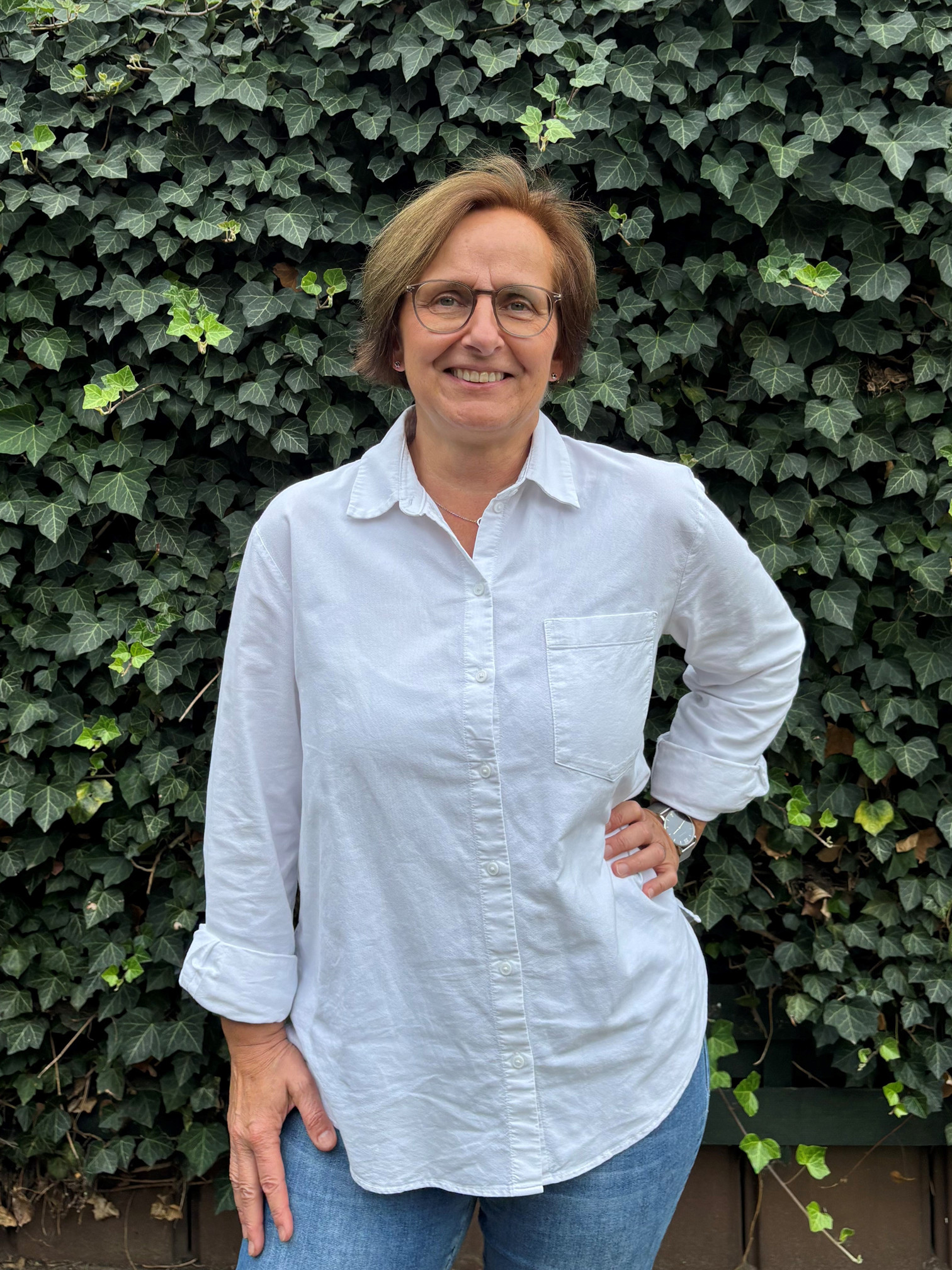 Uta Haffert, Senior Sales Managerin, im weißen Hemd vor einer Efeu-Wand