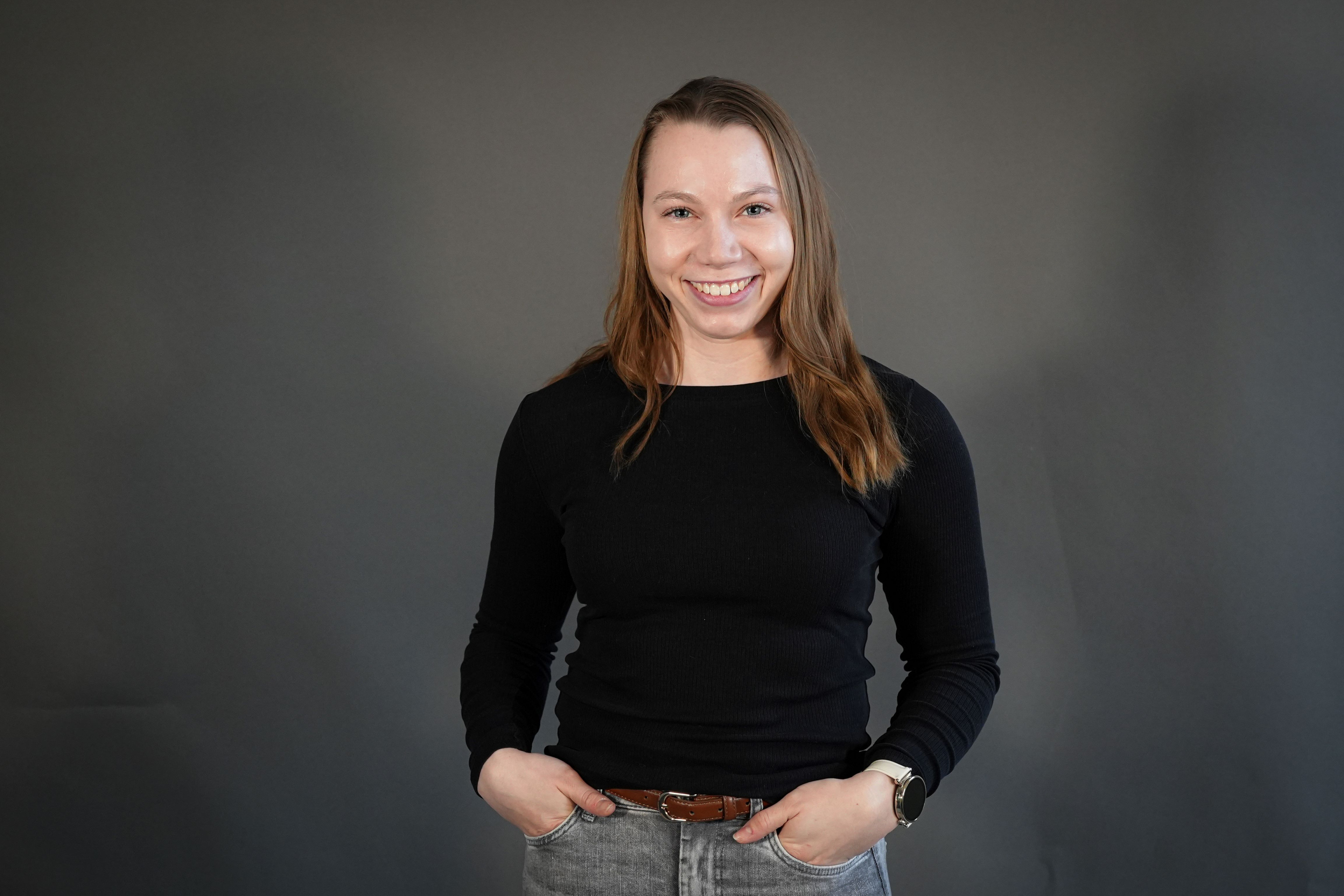 Hannah Garrels in schwarzem Oberteil und grauer Jeans vor grauem Hintergrund