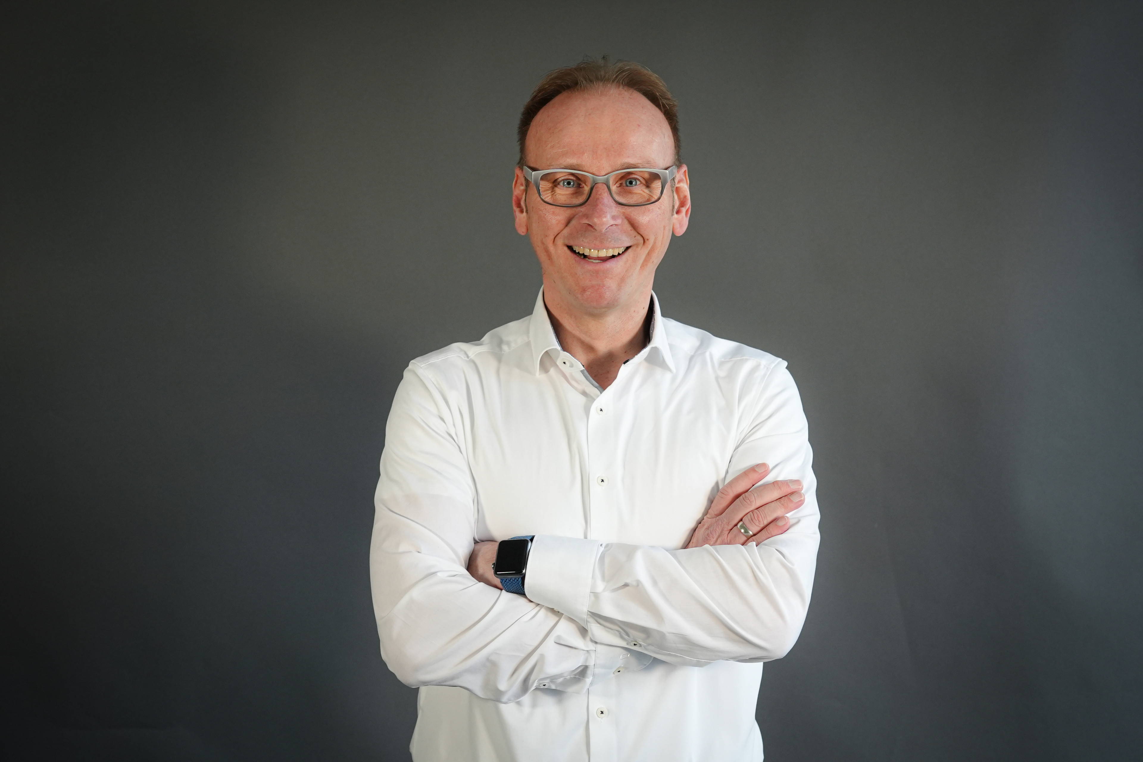 Bert König im weißen Hemd mit verschränkten Armen vor grauem Hintergrund