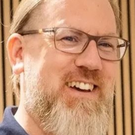 Dr. Au mit Brille und Bart vor einer Holzvertäfelung