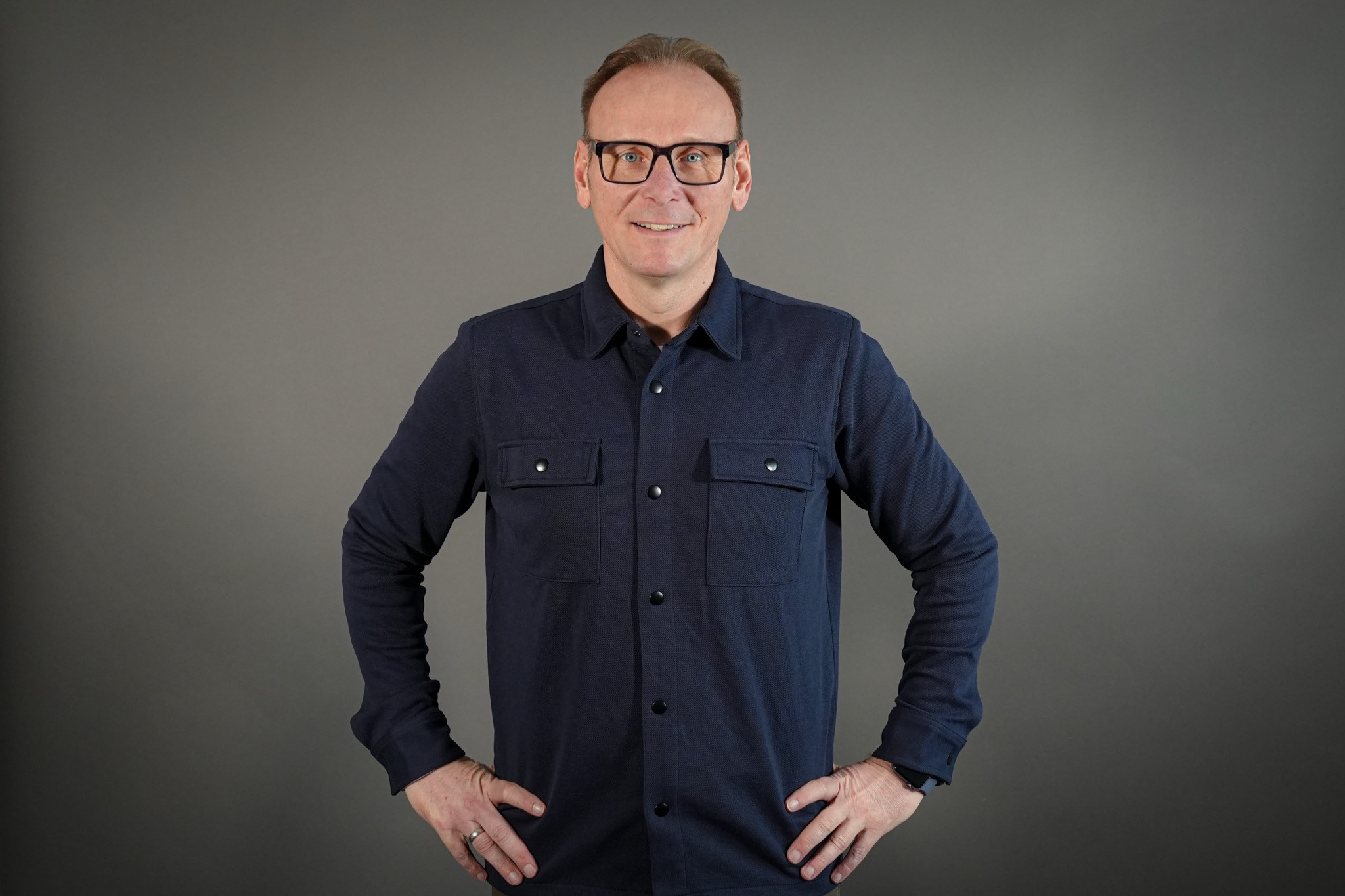 Effiziente Mandantenkommunikation durch juristische Blogs – Mann im blauen Hemd steht mit Händen in der Hüfte vor neutralem Hintergrund