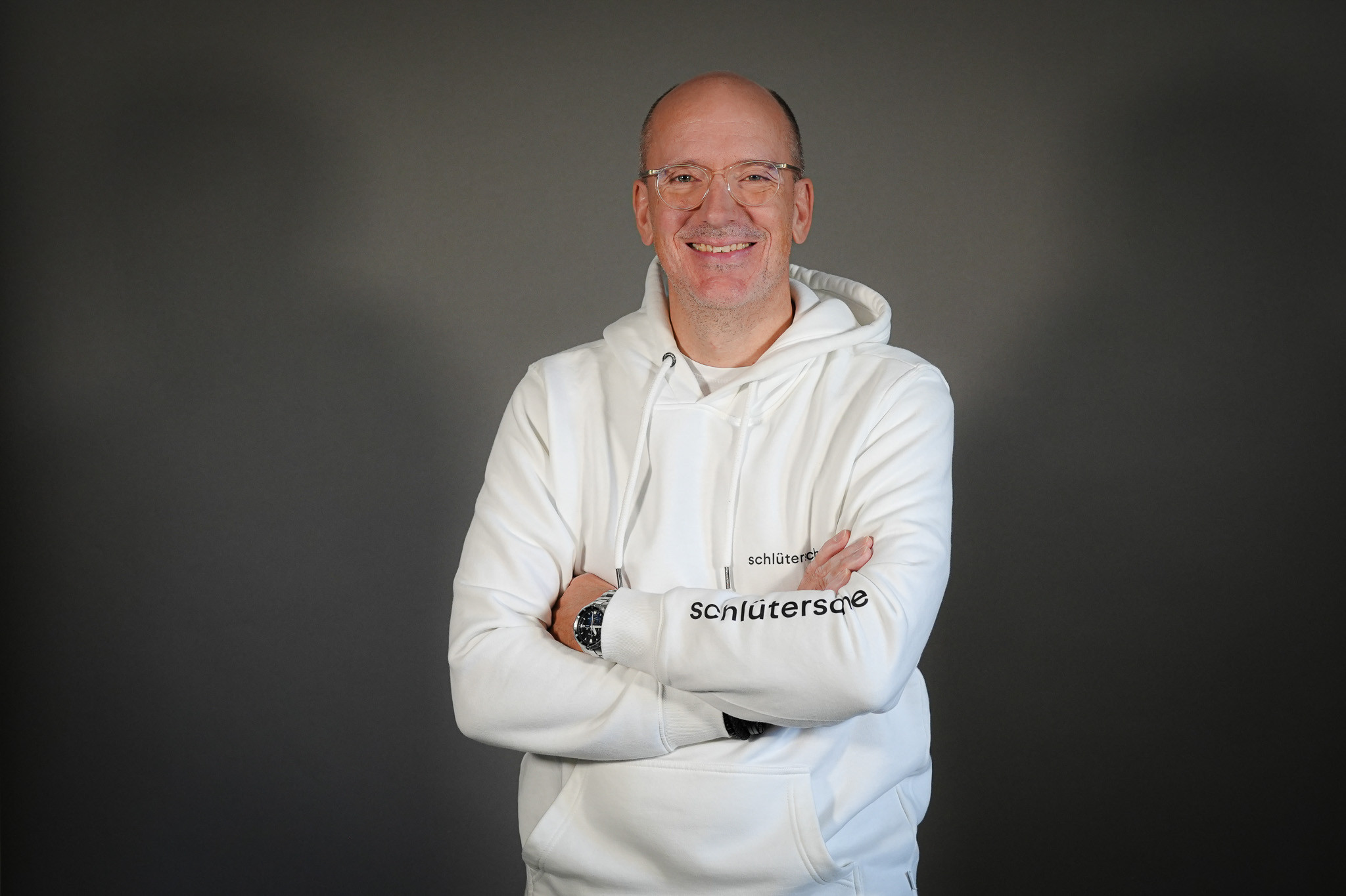Christian Linde im weißen Schlütersche Hoodie mit verschränkten Armen vor grauem Hintergrund