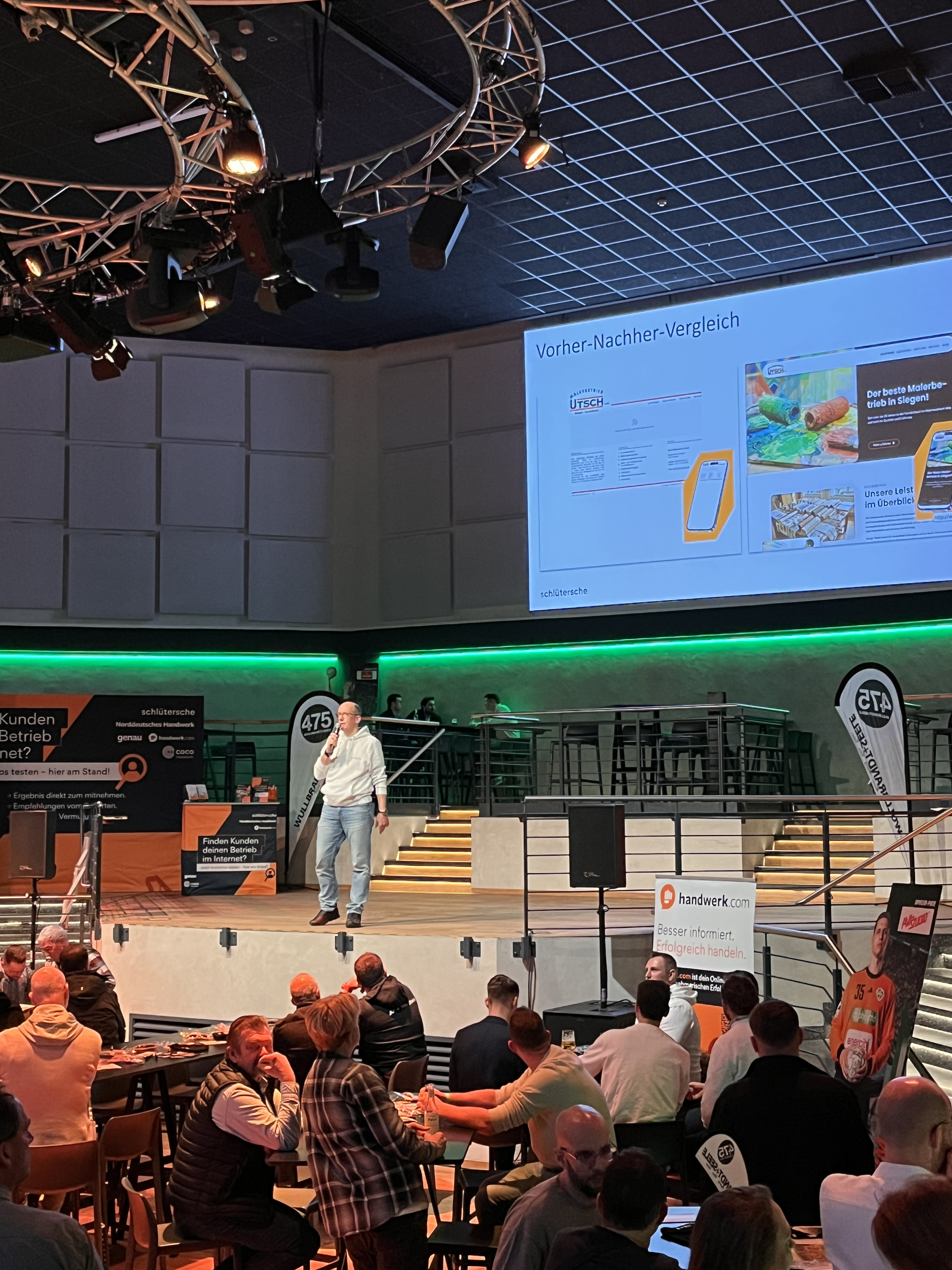Vortrag beim Handwerkerspieltag mit Präsentation zum Vorher-Nachher-Vergleich im Handwerk, Bühne und Publikum im Veranstaltungsraum