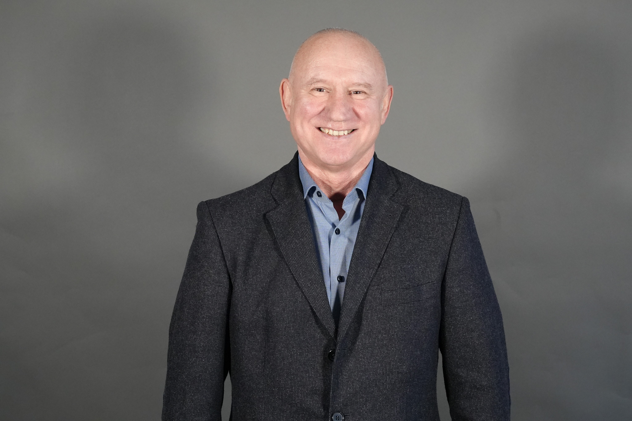 Mario Daquila im Anzug vor grauem Hintergrund