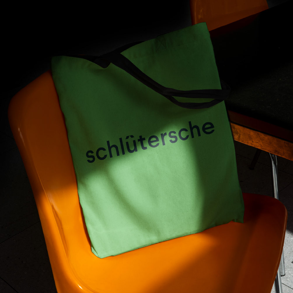 Schl�fctersche Logo auf gr�fcner Stofftasche, fotografiert auf einem orangefarbenen Stuhl