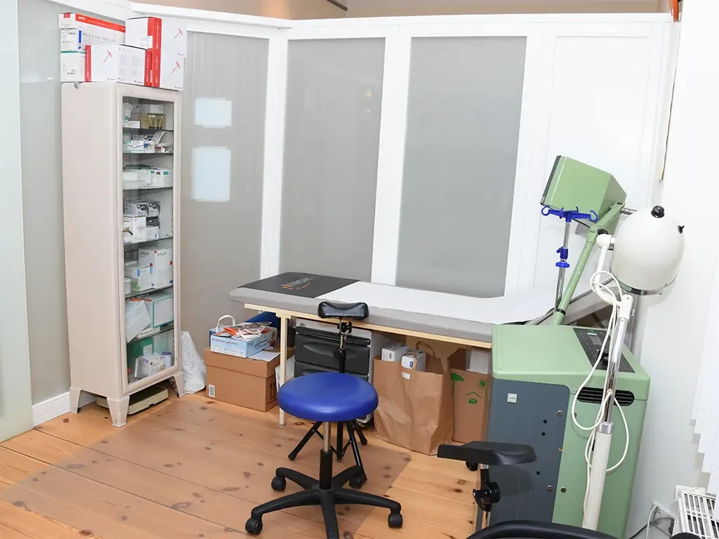 Behandlungszimmer in einer Arztpraxis mit Behandlungsliege, medizinischen Geräten und Medikamentenschrank