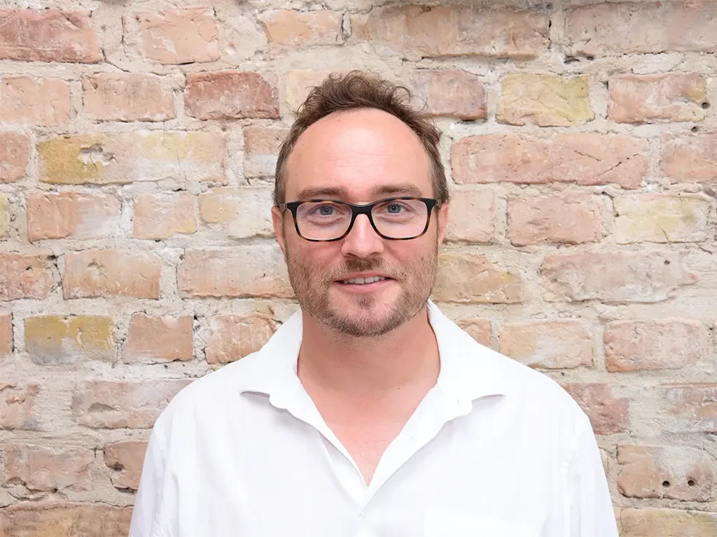 Dr. Felix Lackner vor einer Backsteinwand mit weißem Hemd