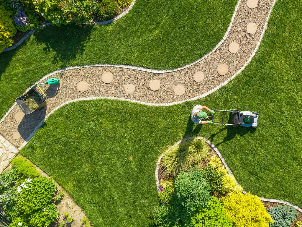 Gartenpflege: Person mäht den Rasen in einem gepflegten Garten mit geschwungenen Wegen