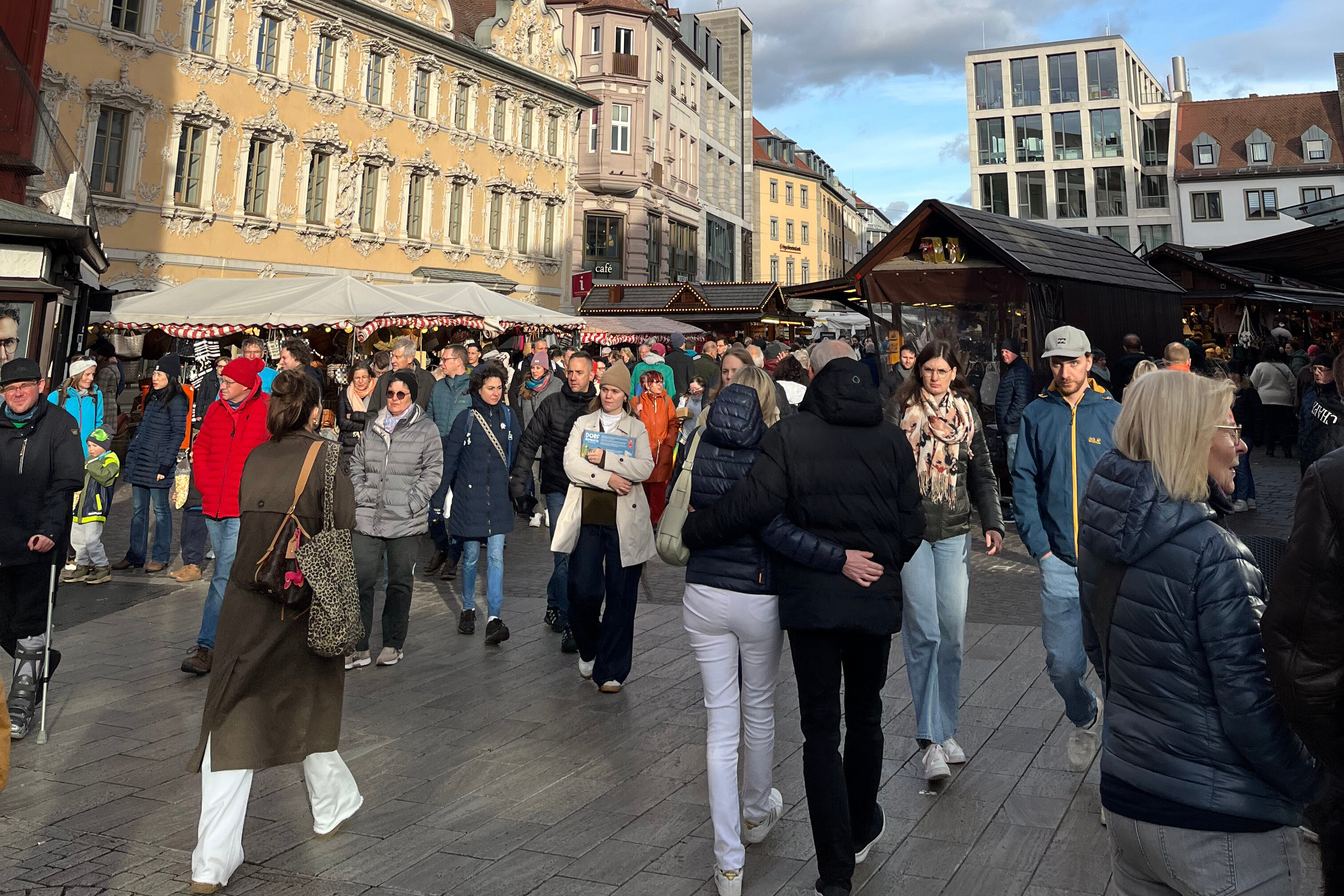Weihnachtsmarkt in der Altstadt mit Menschen und festlich geschmückten Ständen Menschenmenge auf einem Weihnachtsmarkt in einer historischen Altstadt mit festlich geschmückten Buden und barockem Gebäude im Hintergrund