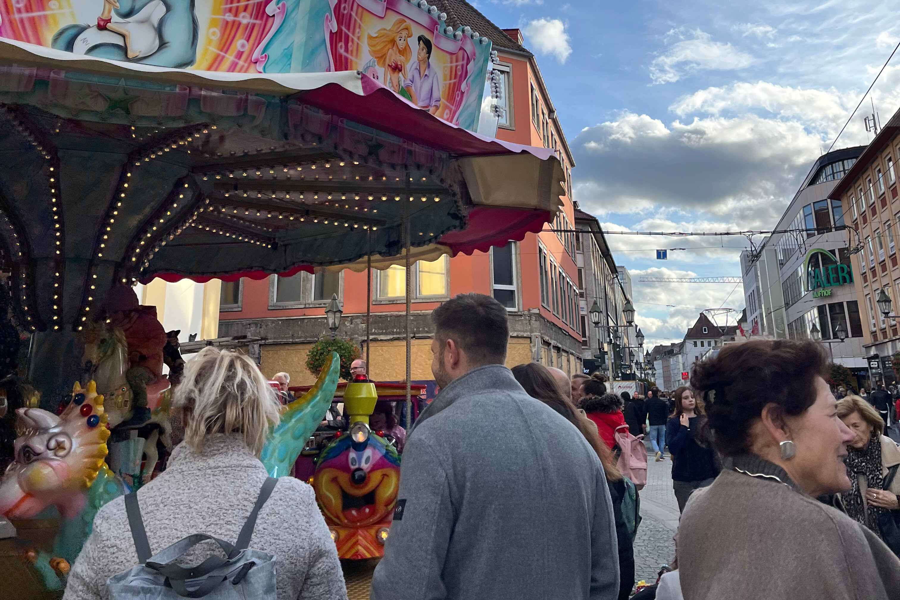 Jahrmarkt mit Karussell in der Innenstadt bei Tag Menschen auf einem Jahrmarkt vor einem Karussell in einer belebten Innenstadt bei Tageslicht