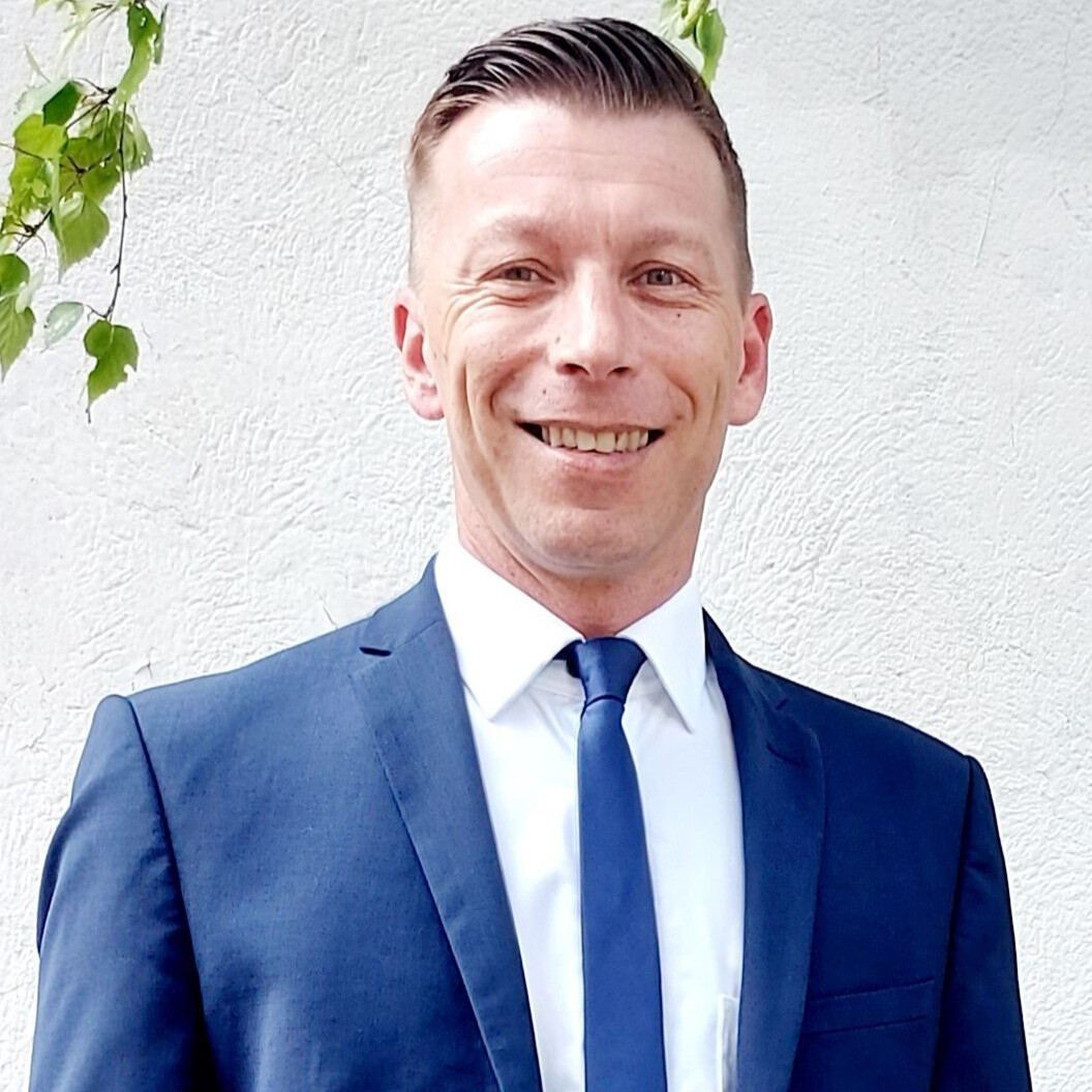 Mann im blauen Anzug mit weißem Hemd und Krawatte vor heller Wand