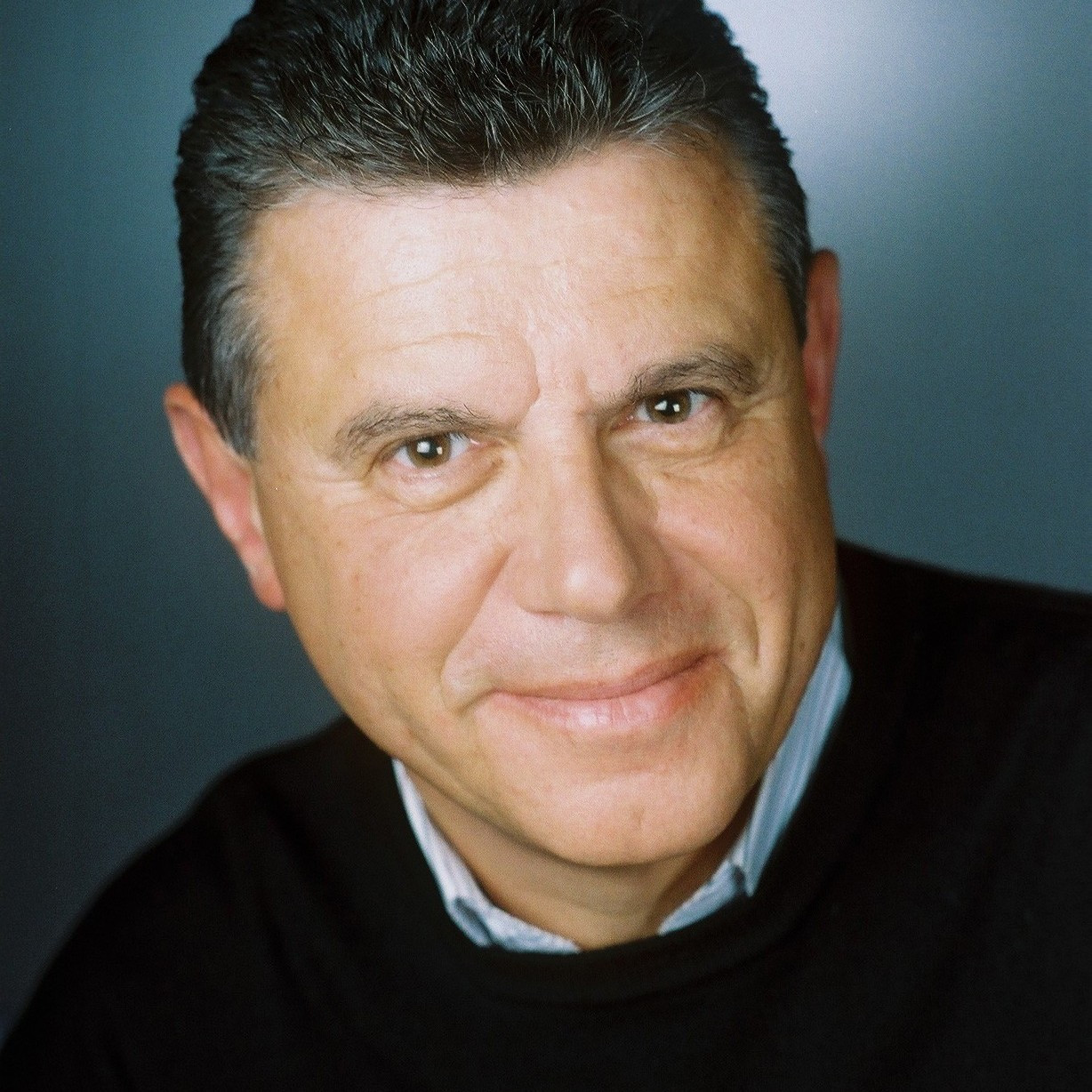 Porträt eines Mannes mit dunklen Haaren und schwarzem Pullover vor neutralem Hintergrund