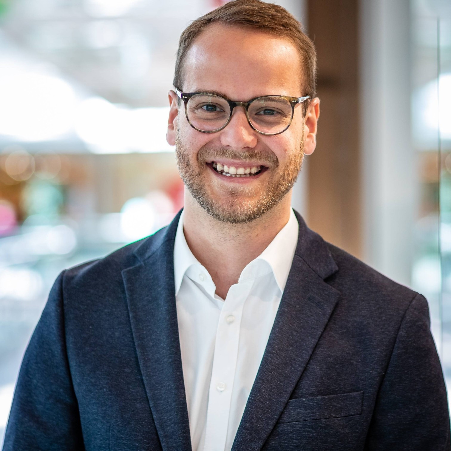 Mann im Business-Outfit mit weißem Hemd und blauem Sakko in modernem Büro