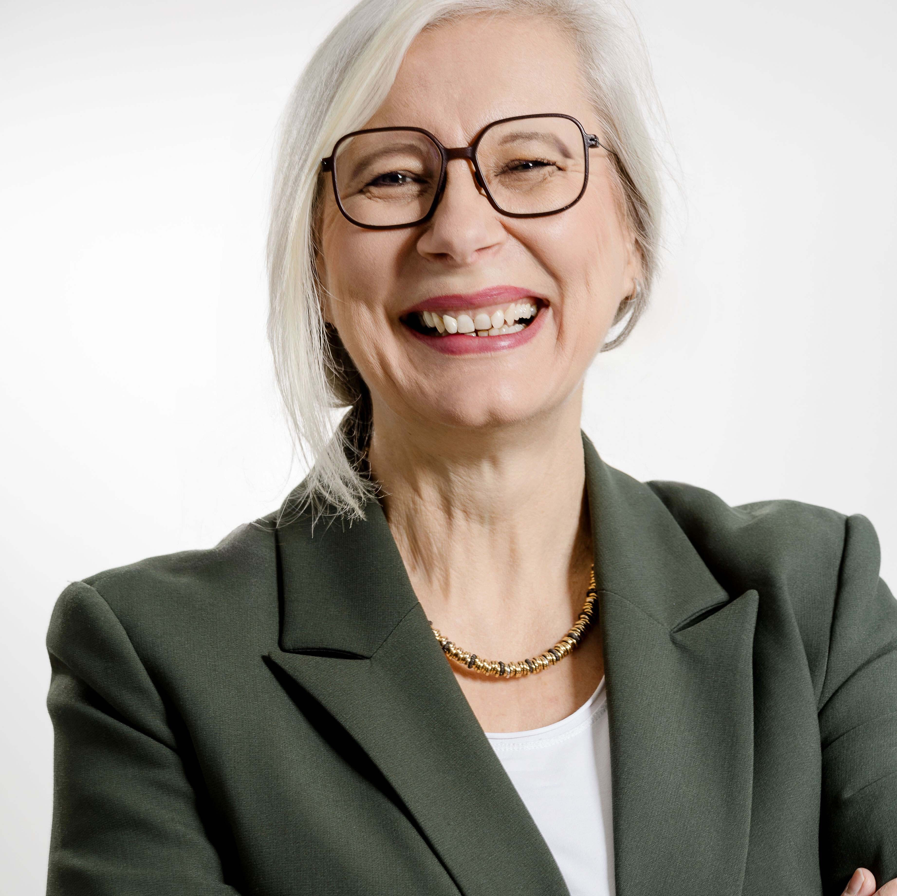 Porträt einer Frau mit grauem Blazer und Halskette vor weißem Hintergrund
