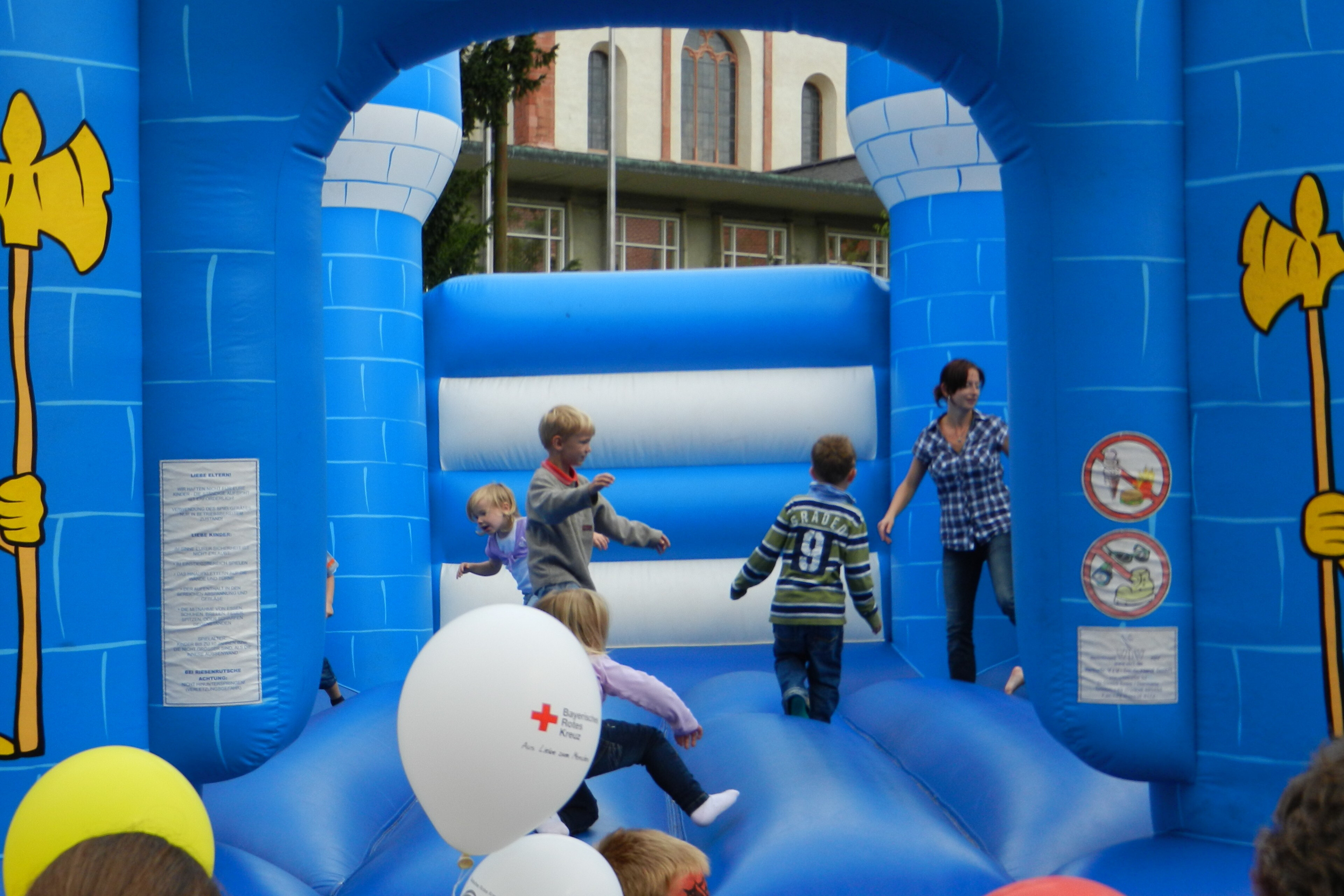 Kinder spielen auf einer blauen Hüpfburg bei einem Fest mit Luftballons des Deutschen Roten Kreuzes