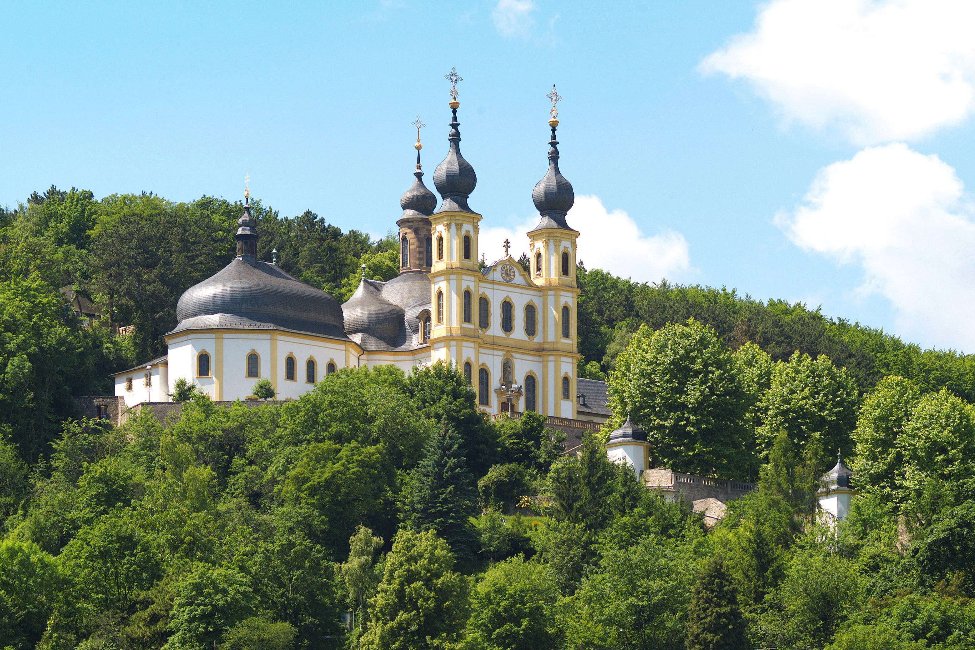 Barocke Kirche auf einem Hügel umgeben von Bäumen und Wald bei blauem Himmel