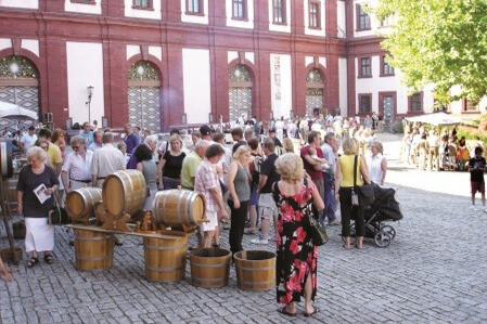 Menschenmenge bei einem Weinfest mit Weinfaessern und Traubenstampfen vor historischem Gebaeude