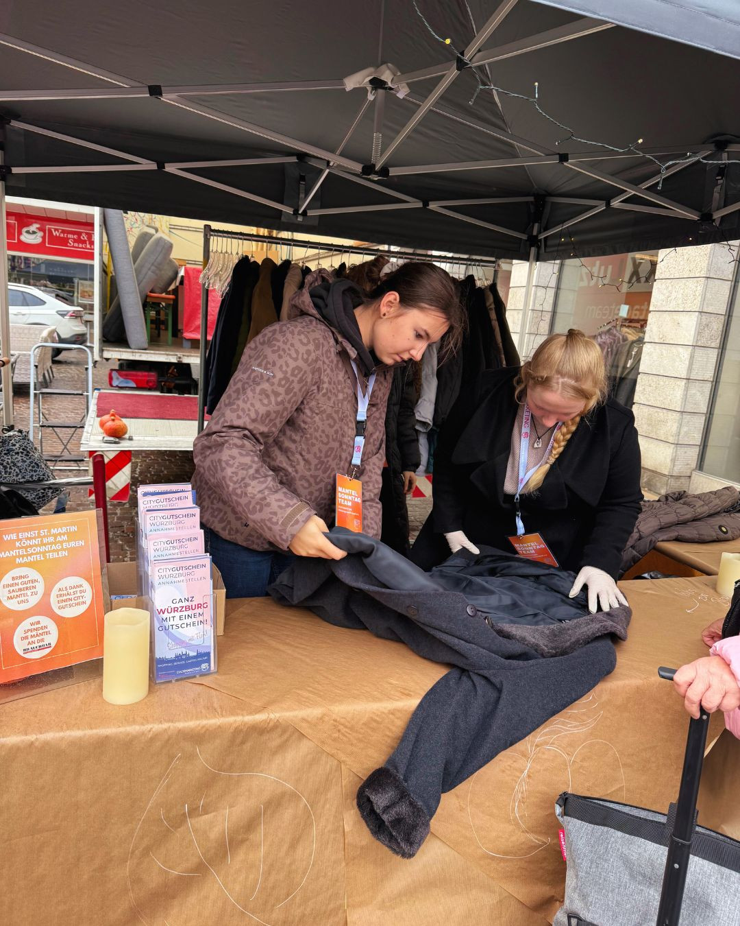 Zwei Frauen beim Mantelsonntag in Würzburg nehmen einen Mantel an einem Spendenstand entgegen.