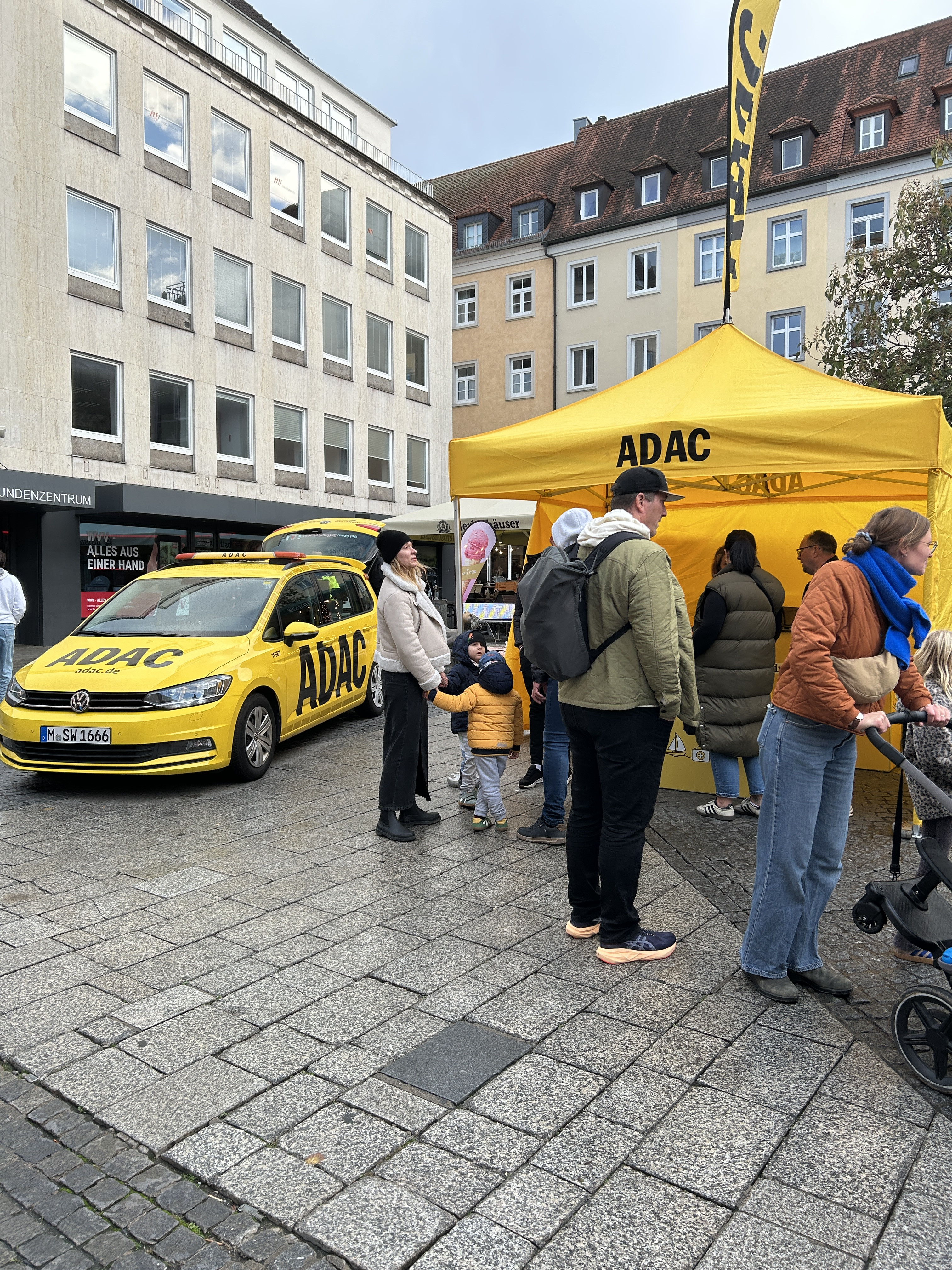 ADAC Infostand mit gelbem ADAC Auto und Besuchern in der Innenstadt