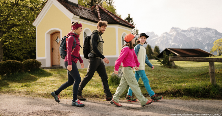 Familie beim Wandern vor einer gelben Kapelle in den Bergen