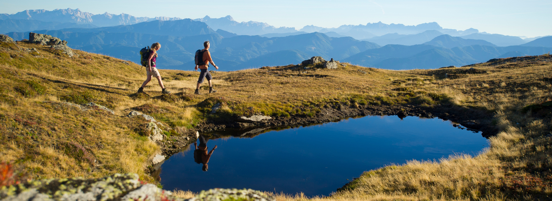 Wanderer mit Rucksack in den Bergen neben einem kleinen See, Panorama mit Alpen im Hintergrund