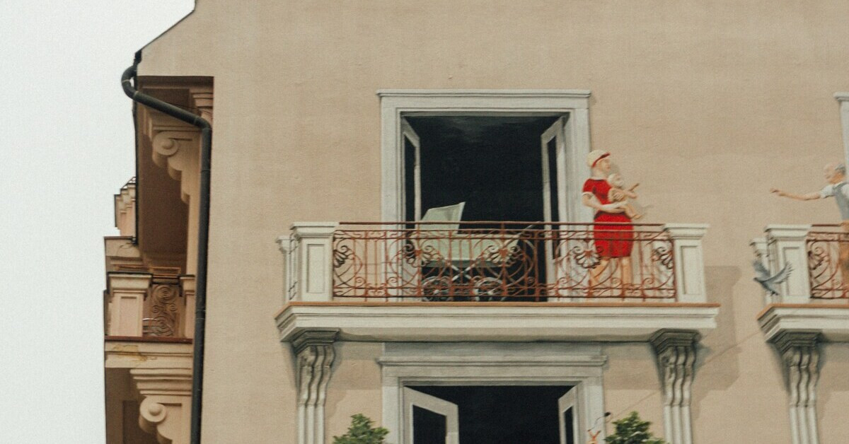 Illusionsmalerei eines Balkons mit Frau und Kinderwagen an einer Hausfassade