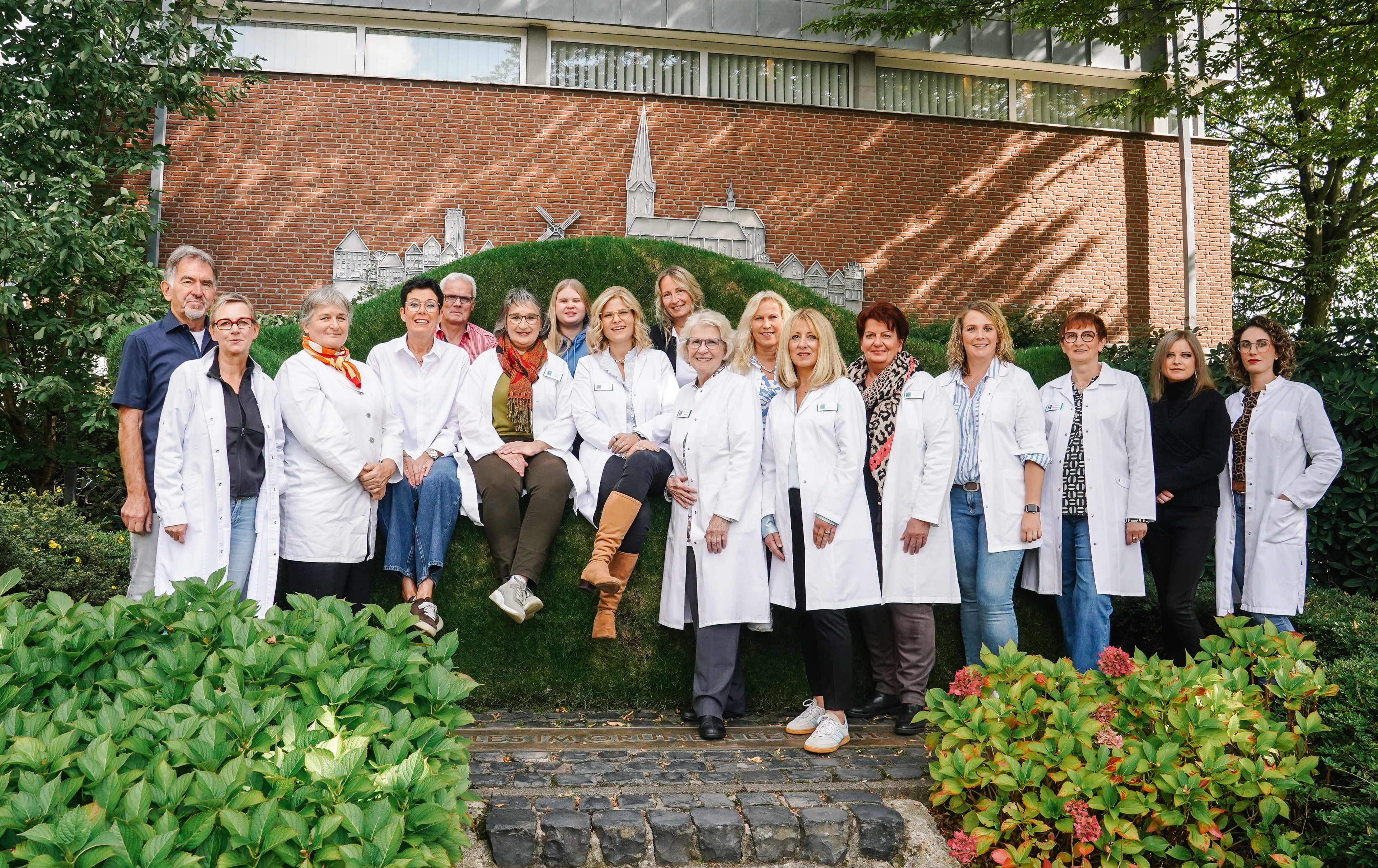 Gruppenfoto von Mitarbeitern im weißen Kittel vor einer Backsteinwand, aufgenommen vom Fotostudio Kaufels