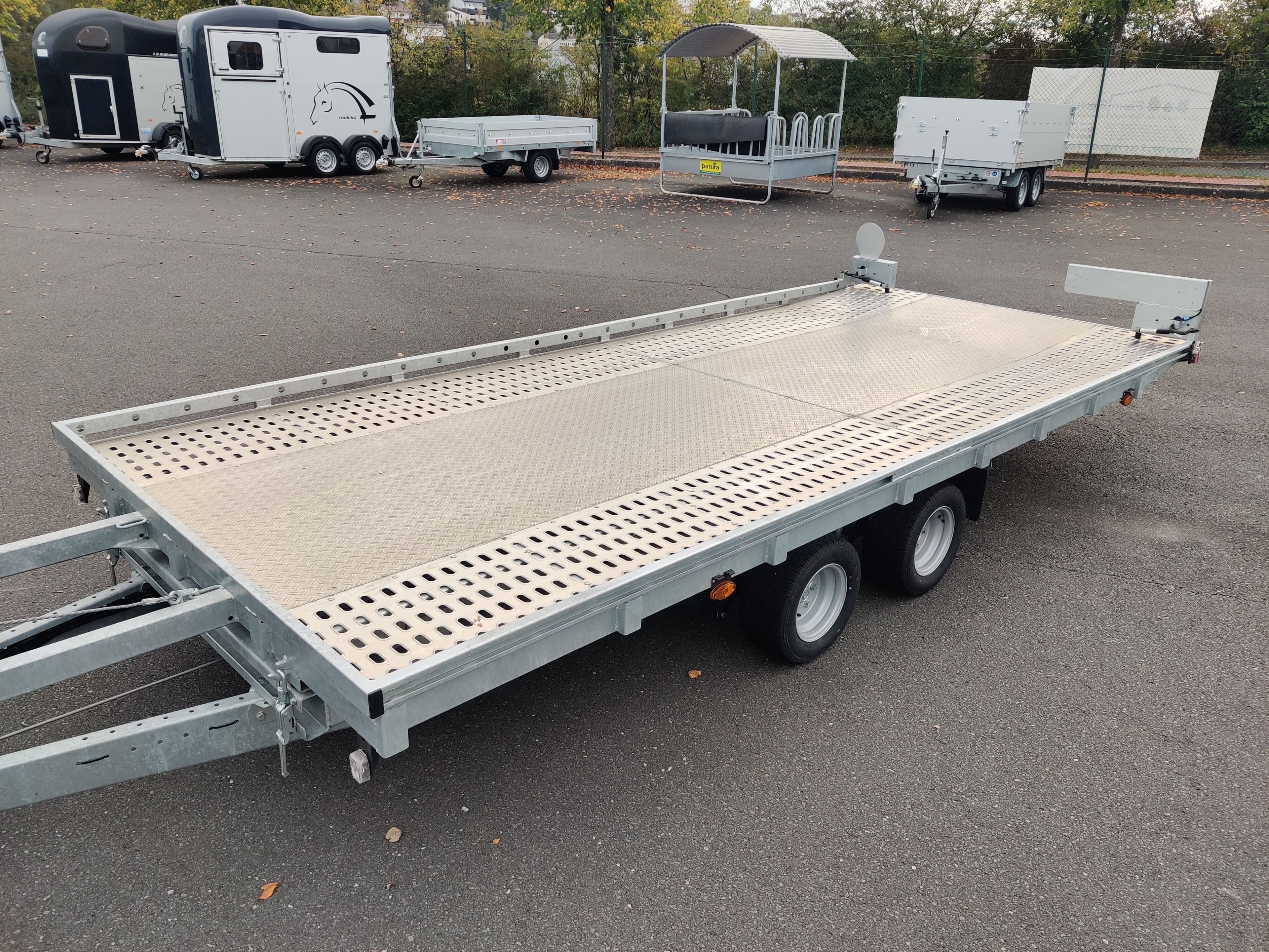 Farmperfekt Anhängervermietung – Autotrailer mieten auf dem Parkplatz, verschiedene Anhänger im Hintergrund