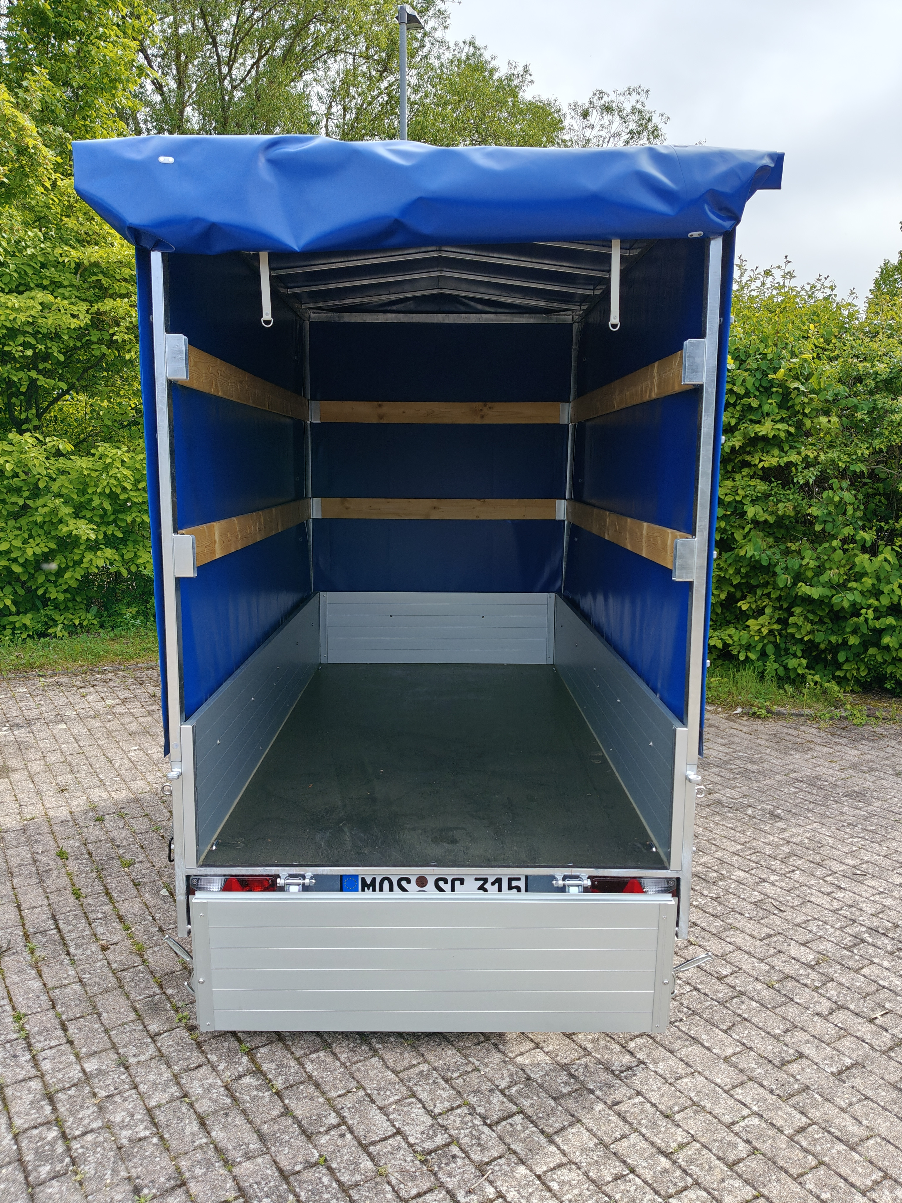 Innenansicht eines leeren, mit blauer Plane abgedeckten Anhängers auf Pflasterfläche
