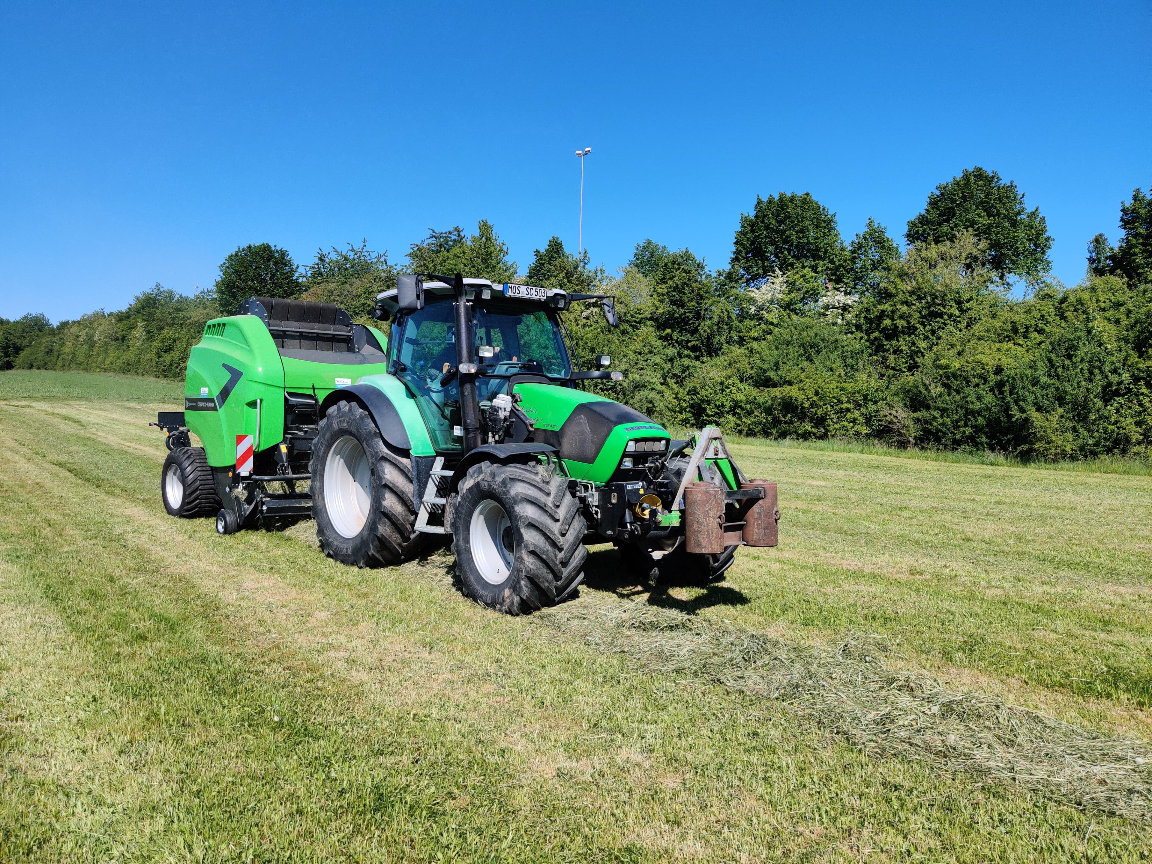 Grüner Traktor mit Ballenpresse auf einer Wiese bei Sonnenschein