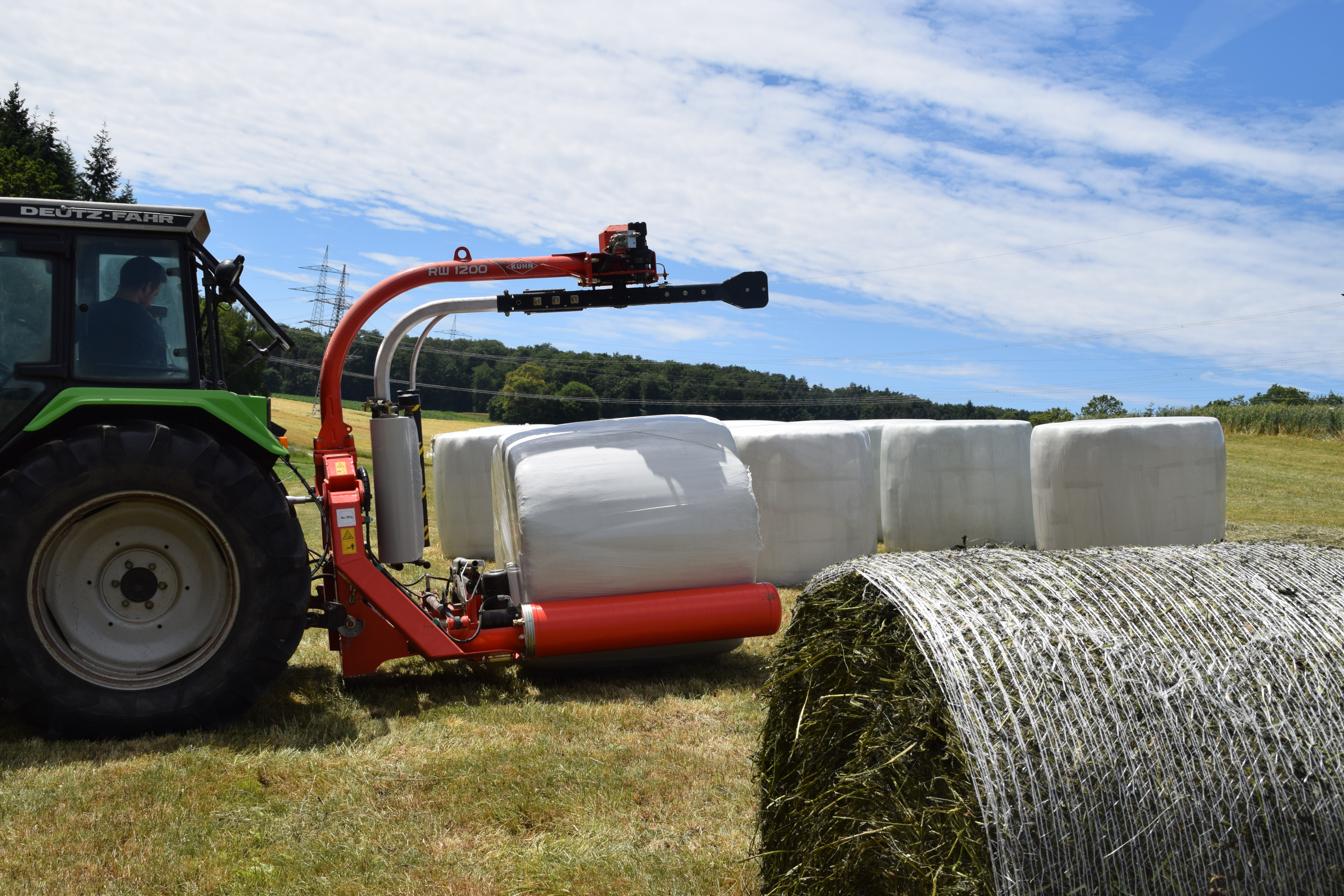 Traktor mit Ballenwickler und Silageballen auf einer Wiese bei der Heuernte