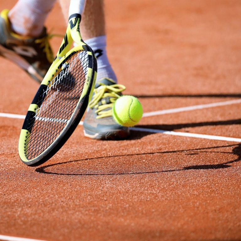 Tennisspieler beim Schlag auf Sandplatz mit gelbem Tennisball und Tennisschläger