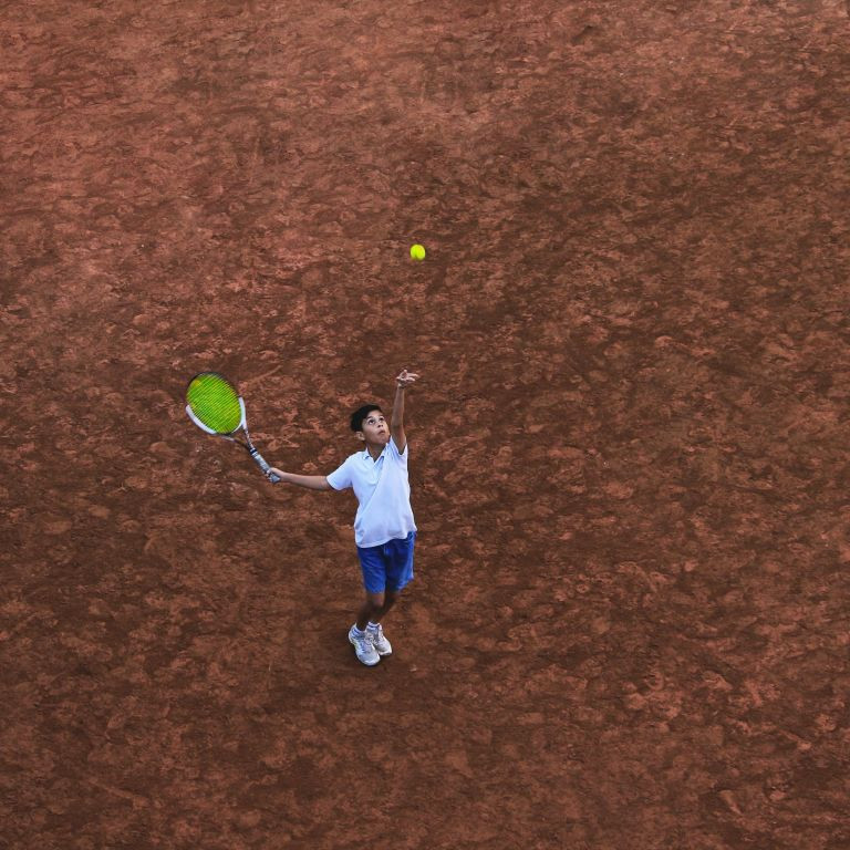 Tennis-Kid beim Aufschlag auf Sandplatz