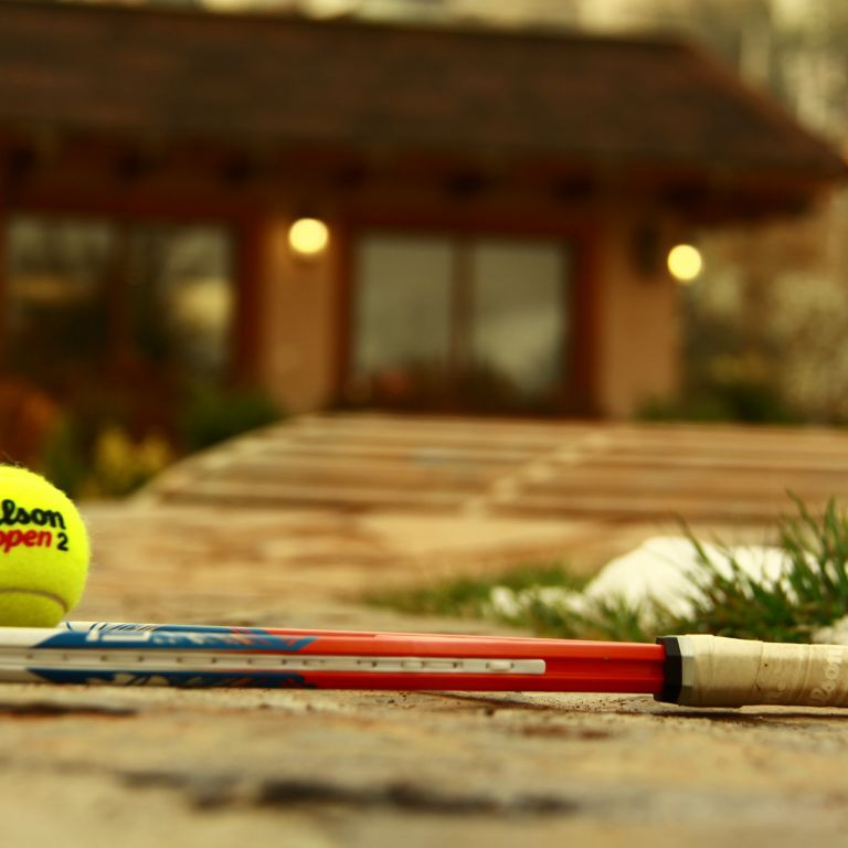 Tennis-Gast mit Tennisschläger und Wilson Open 2 Tennisball vor einem Haus