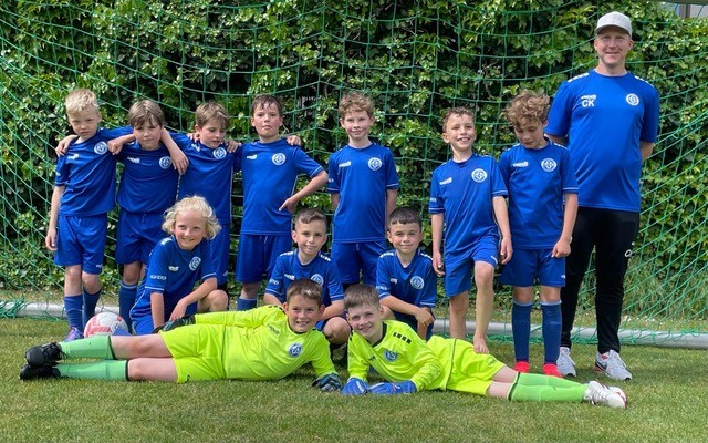 Gruppenfoto eines Jugendfußballteams in blauen Trikots vor einem Fußballtor