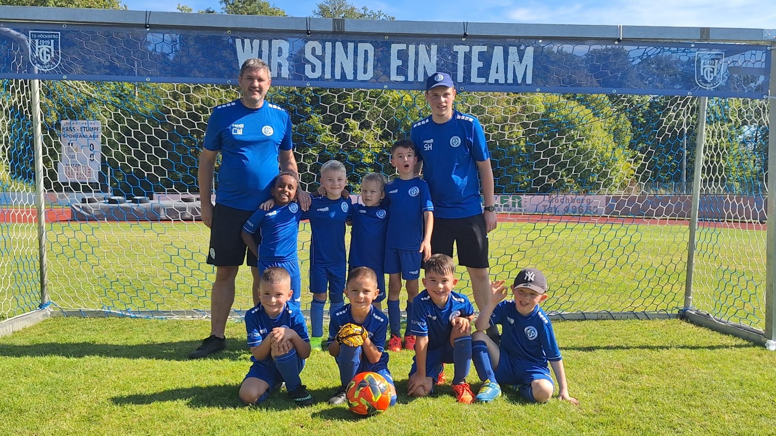 Jugendfußballmannschaft mit Trainern vor einem Tor mit dem Schriftzug 'Wir sind ein Team'