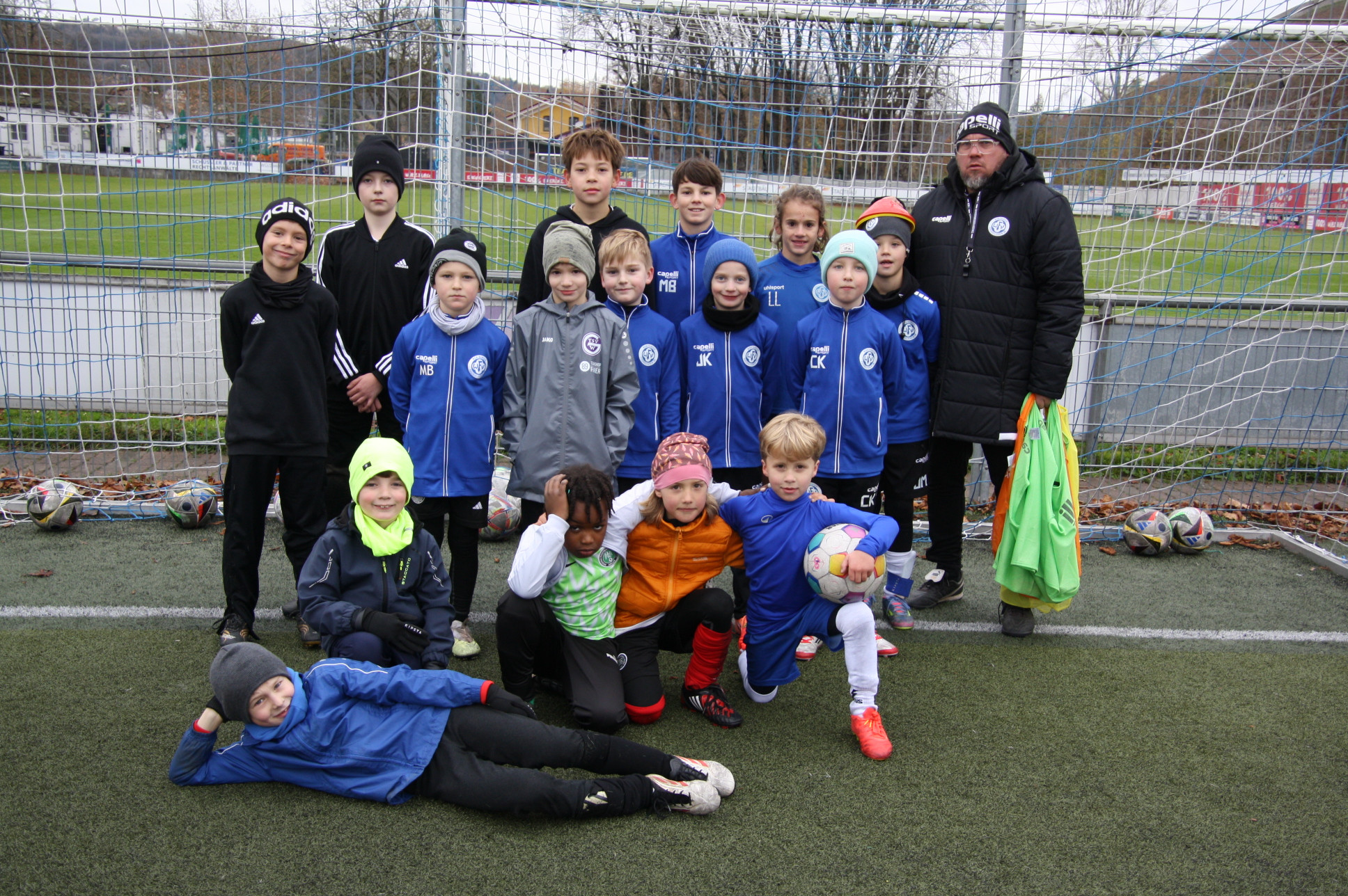 Kinderfußballmannschaft mit Trainer auf dem Sportplatz vor dem Tor