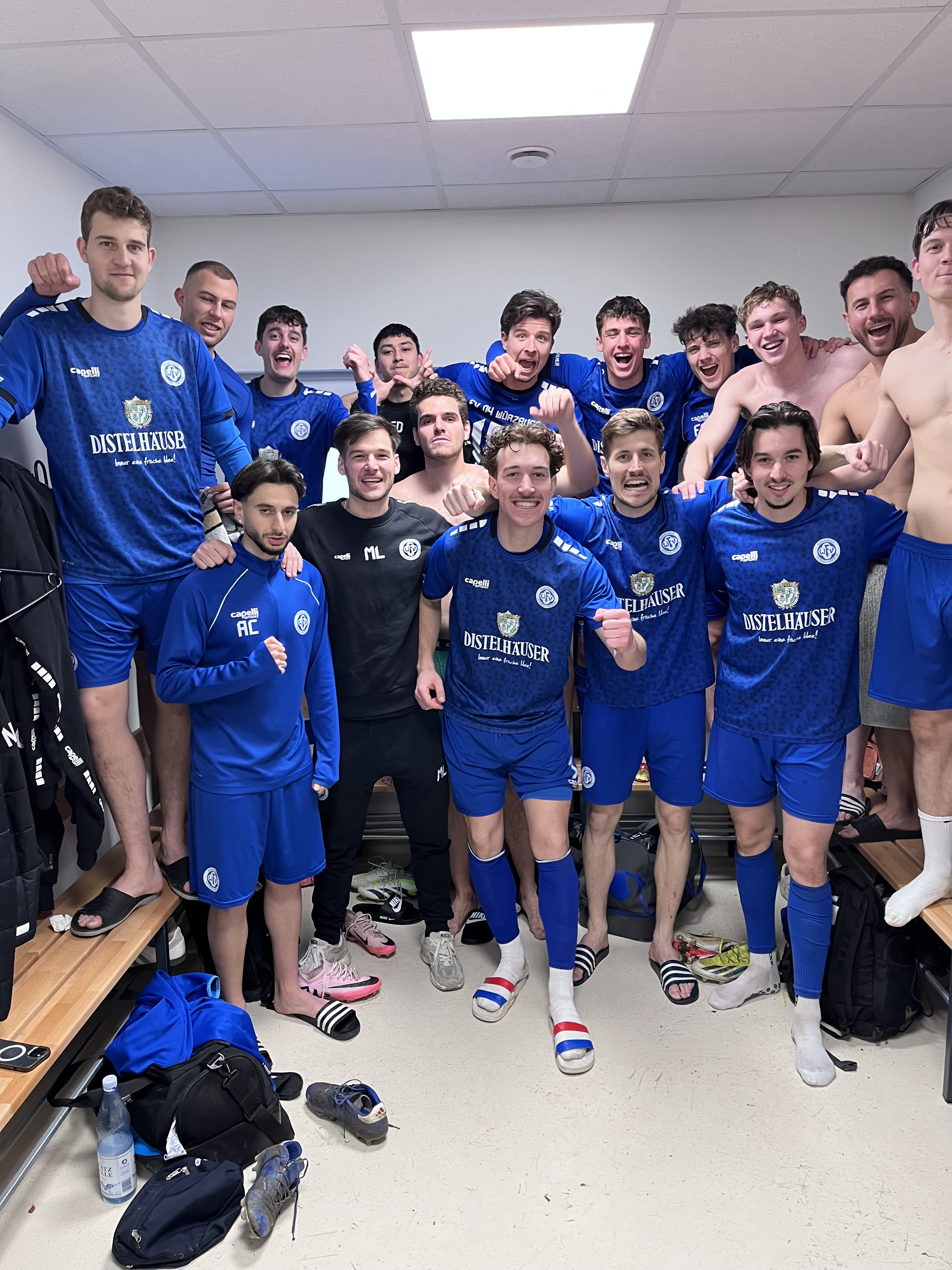 Fußballmannschaft jubelt im Umkleideraum nach dem Spiel, Spieler in blauen Trikots mit Distelhäuser Logo