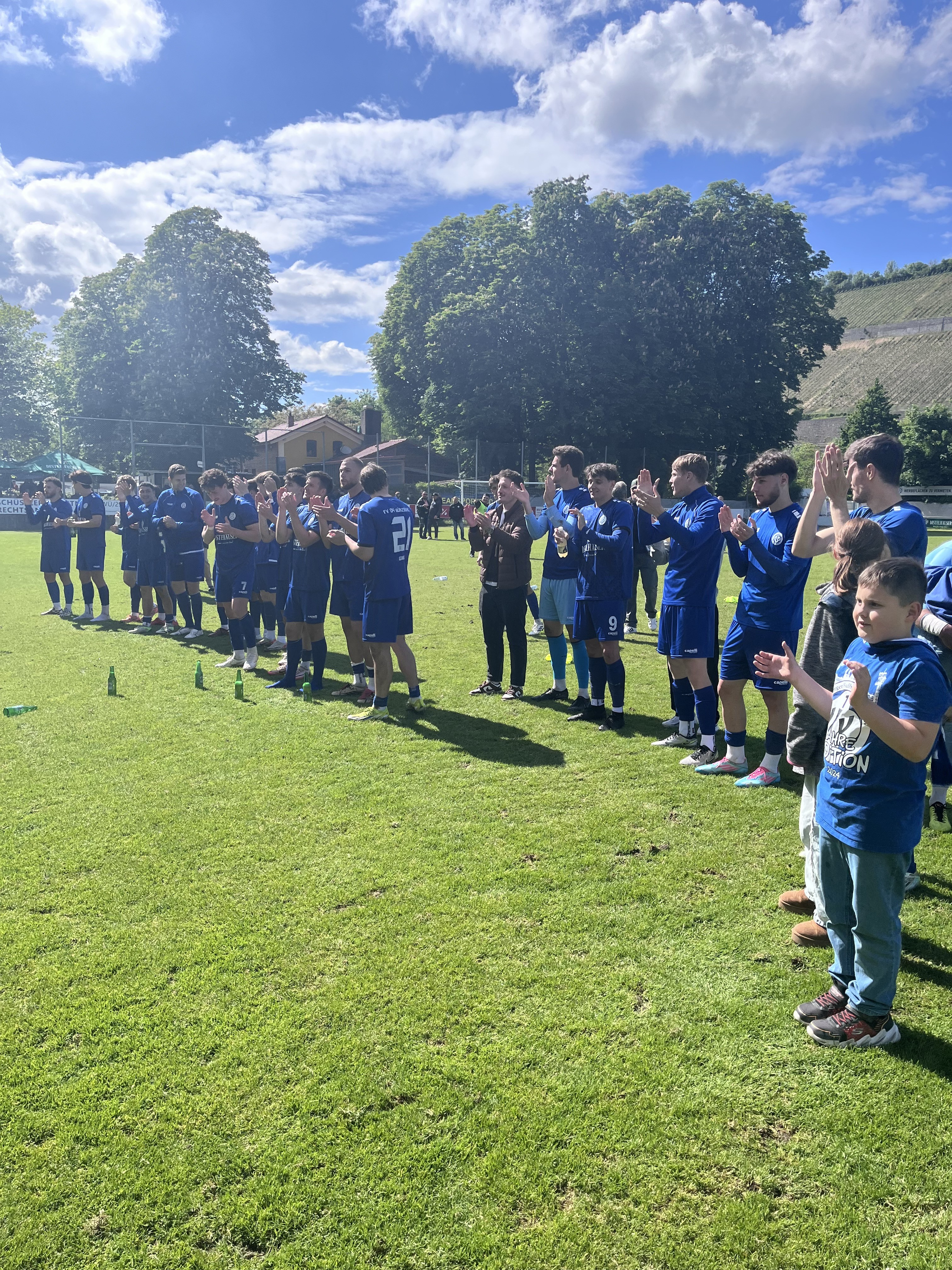 Fußballmannschaft in blauen Trikots feiert auf dem Spielfeld nach einem Spiel bei sonnigem Wetter
