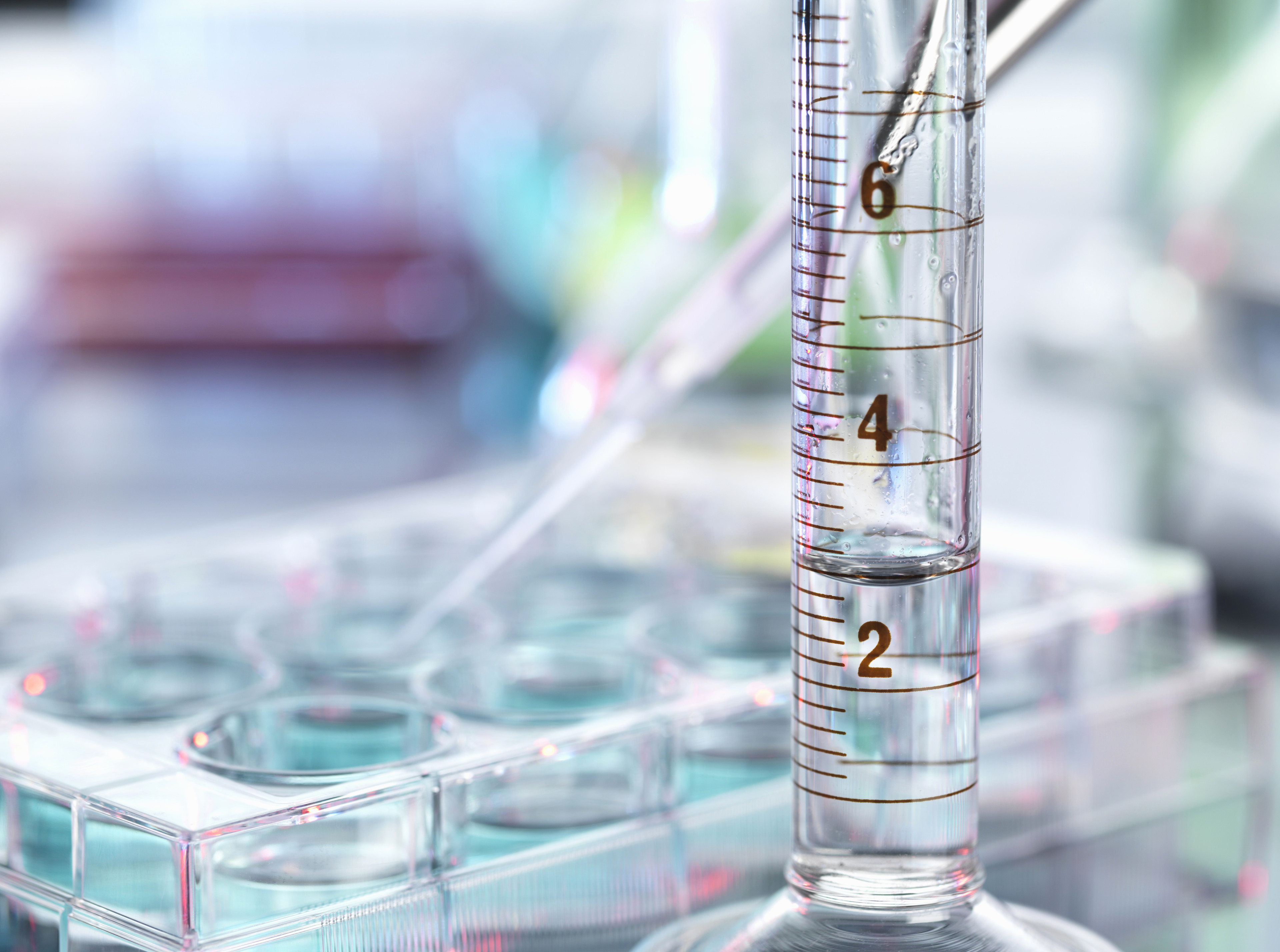 Messzylinder und Pipette im Labor mit Zellkulturplatten im Hintergrund